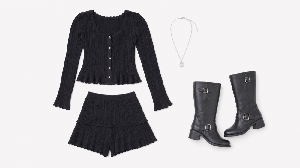 The wardrobe laid flat on white: a black ribbed button-front cardigan, matching ruffled shorts, a silver pendant necklace and black leather buckle boots